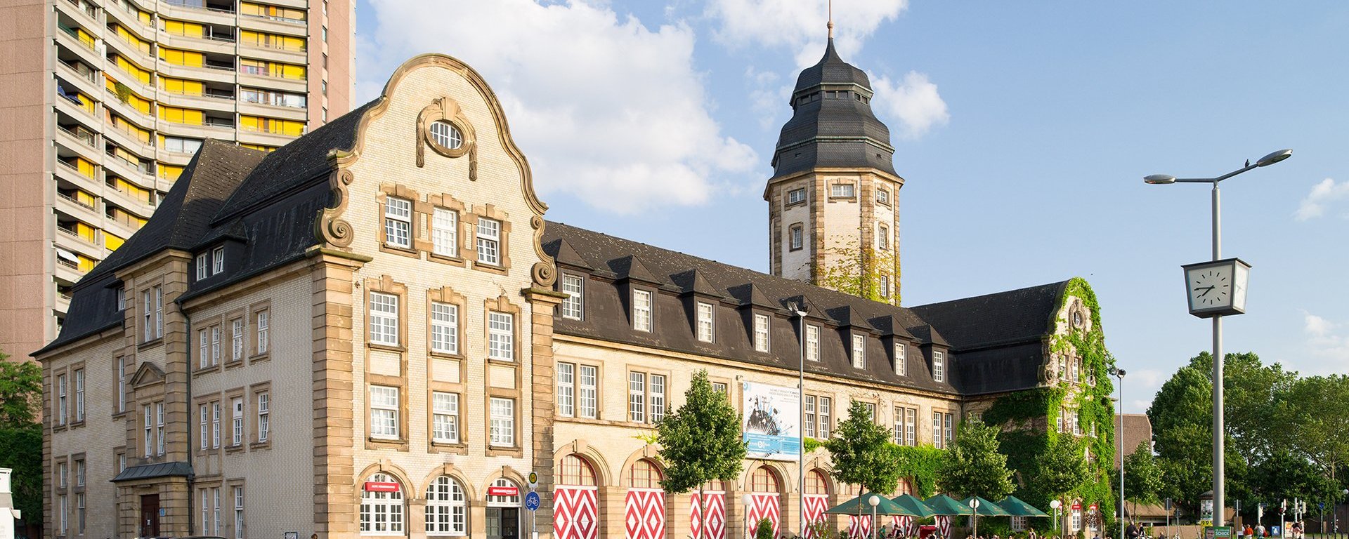 Außenansicht eines Einsatzgebäudes an einer Straße mit vorbeifahrenden Fahrradfahrern.