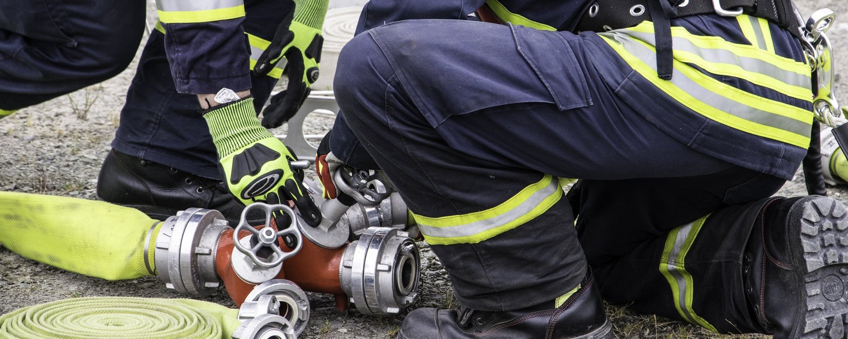 Zwei Feuerwehrmänner in Einsatzkleidung Schrauben an einem Ventil eines Wasserschlauchs.
